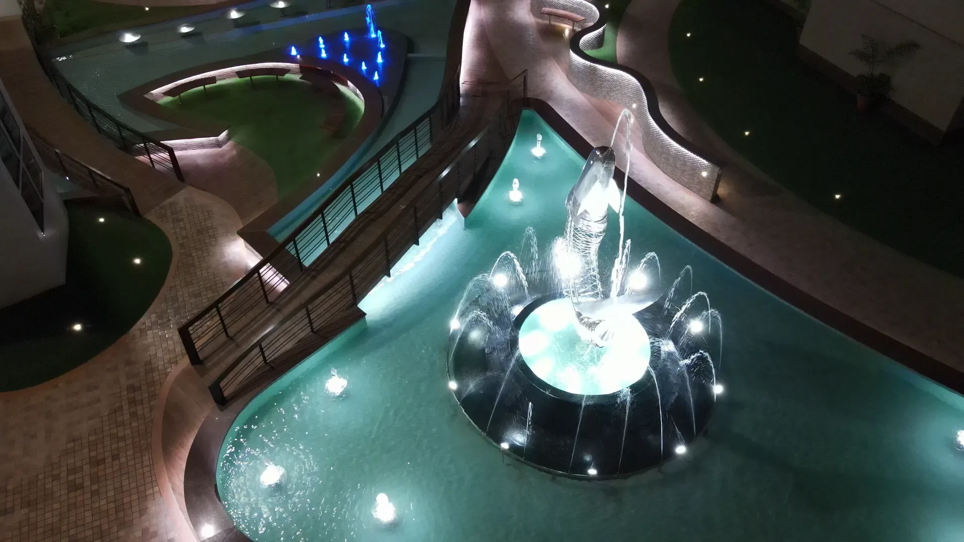 The fountain at night, water lit from below.