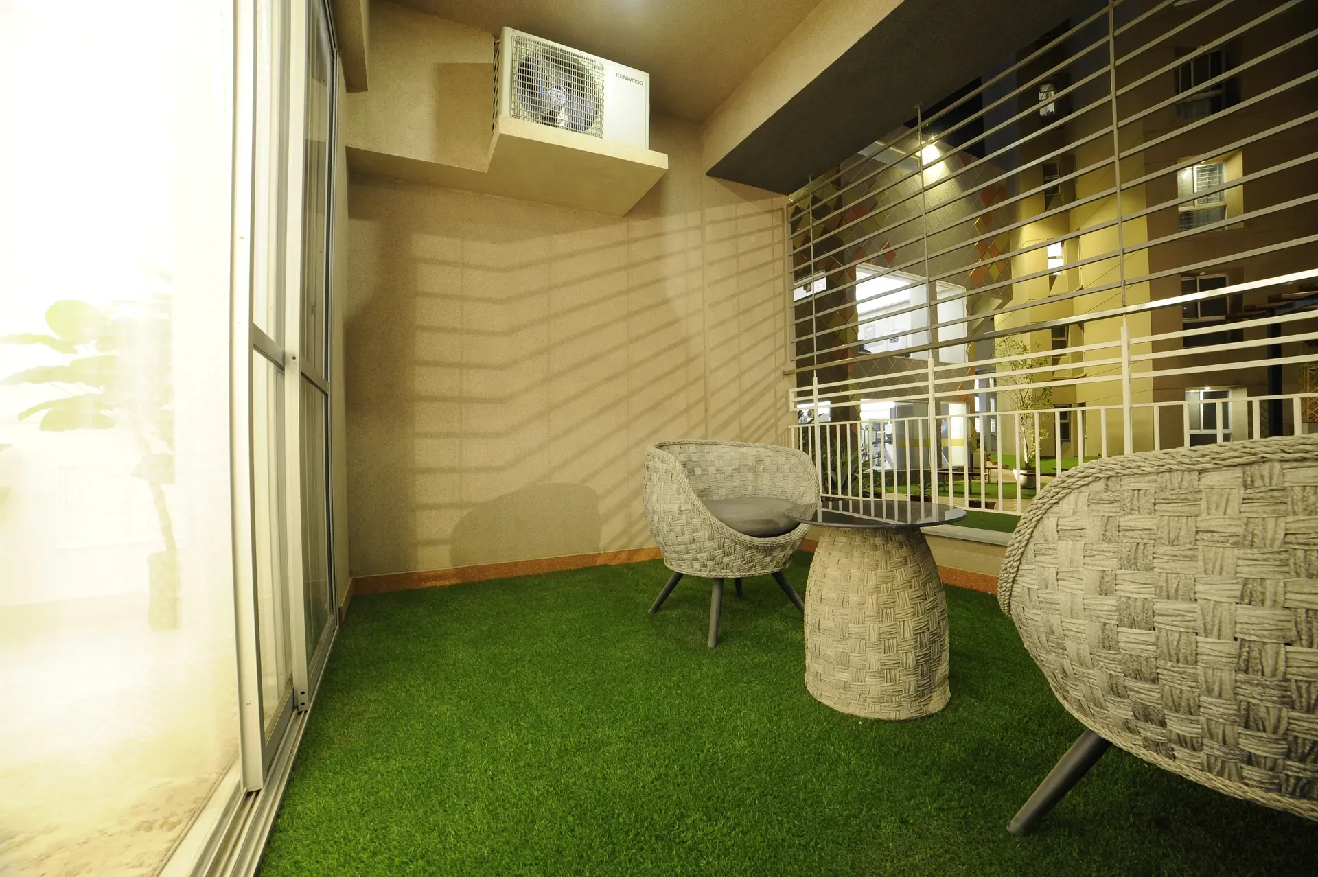 A private terrace laid to lawn, woven chairs and a low table under the screen.